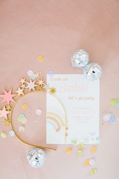 some confetti and stars on a pink table with a white card that says barbieie let's go party