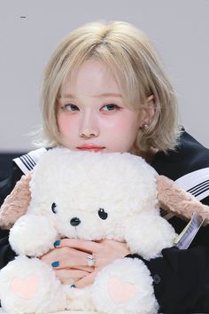 a young woman holding a white teddy bear in her hands and looking at the camera