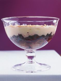 a dessert in a glass bowl on top of a white tablecloth with purple background