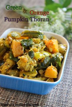 green and orange pumpkin thoran is in a blue dish on a table with flowers