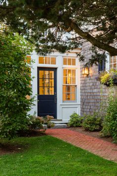 a house with a blue front door and brick walkway leading to the side entrance, surrounded by greenery