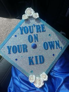 a blue graduation cap that says you're on your own kid with white roses