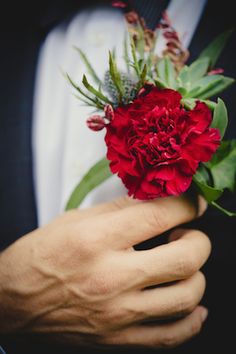 a close up of a person wearing a suit and holding a red flower in his hand