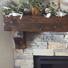 a mantel decorated with pine cones and greenery on top of a stone fireplace