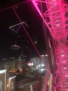 pink lights are shining on the side of a tall building at night with skyscrapers in the background