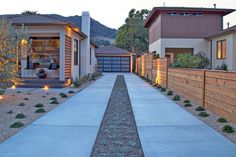 a driveway leading to a house with lights on the side and landscaping in front of it