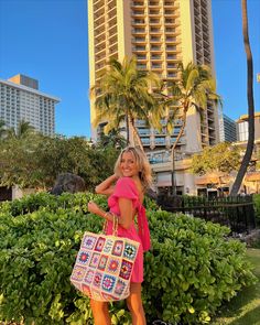 a woman is standing in front of some bushes and palm trees holding a handbag