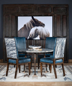 a dining room table with blue chairs and a horse painting on the wall behind it