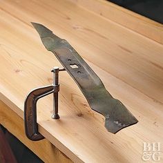 a knife is attached to a piece of metal on a wooden table top with a wrench