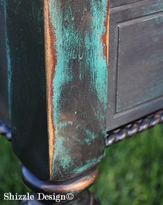 an old wooden table with green and brown paint on it's sides, sitting in the grass