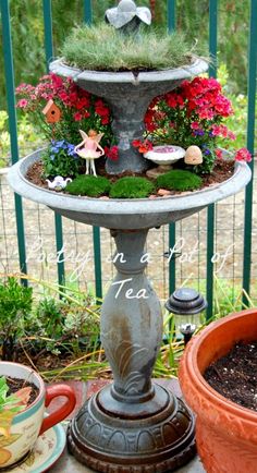 a birdbath filled with flowers and plants on top of a table