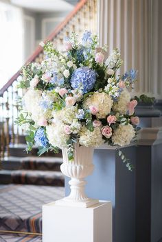 a vase filled with white and blue flowers on top of a table next to a stair case