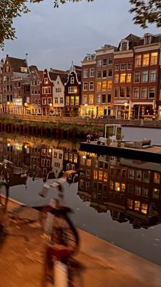 a bicycle parked on the side of a river next to tall buildings at night time