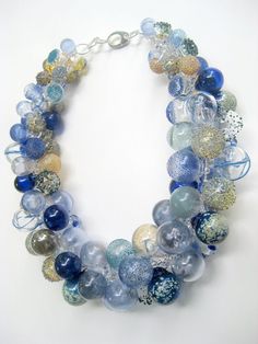 a necklace made out of glass beads on a white surface with silver and blue accents