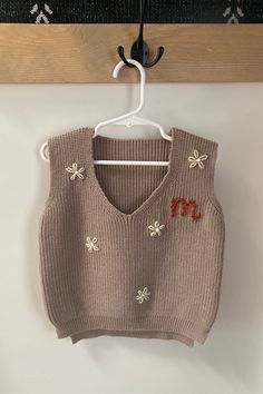 a brown sweater vest hanging on a wooden hanger next to a white coat rack