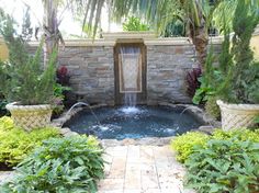 a small pool with a waterfall in it surrounded by greenery and palm tree's