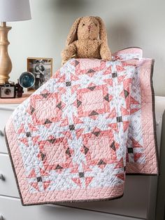 a teddy bear sitting on top of a bed next to a pink and white quilt