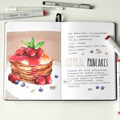 an open book with a drawing of pancakes and cherries on it, next to markers