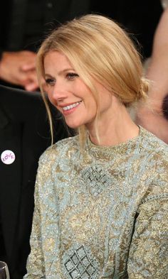 a woman sitting at a table with a glass of wine in front of her smiling