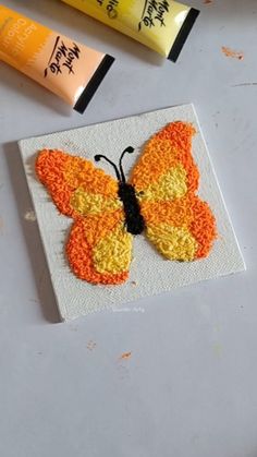 an orange and yellow butterfly sitting on top of a piece of paper next to some glue