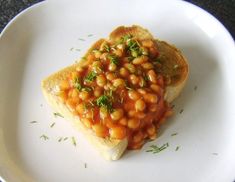 a white plate topped with two pieces of toast covered in baked beans and garnish