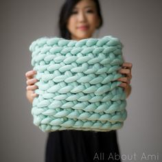 a woman holding up a large knitted pillow