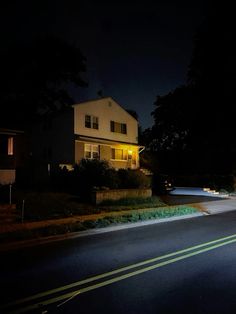 an empty street at night with a house in the background and light shining on it