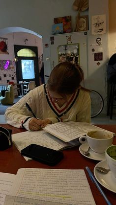 a woman sitting at a table writing on paper with a cup of coffee in front of her