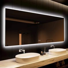 two sinks in front of a large mirror with lights on the wall above it and below them