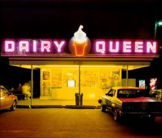 the dairy queen is lit up at night with neon signs on it's front