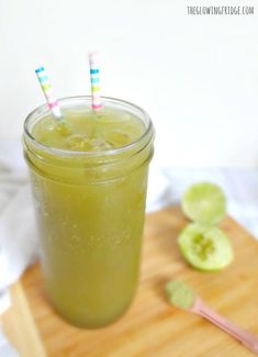 a green drink with two striped straws in a mason jar on a cutting board