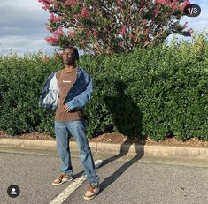 a man standing in the middle of a parking lot next to a tree and bushes