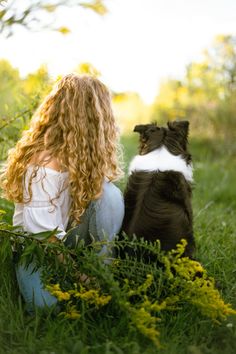 a woman sitting in the grass next to a black and white dog with long curly hair