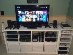 a flat screen tv sitting on top of a white entertainment center next to shelves filled with electronics