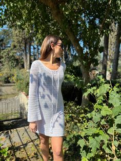 a woman standing in front of a tree wearing glasses and a white dress with long sleeves