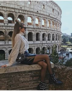 a woman sitting on top of a stone wall next to an amphite building