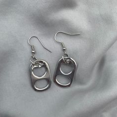 two pairs of silver earrings sitting on top of a white cloth covered bed sheet, with one pair dangling from the ear