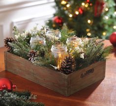 a wooden box filled with mason jars sitting on top of a table next to a christmas tree