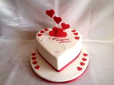 two heart shaped cakes sitting on top of a white tablecloth covered table with red hearts