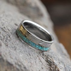 a wedding band with turquoise and gold inlays sits on a rock