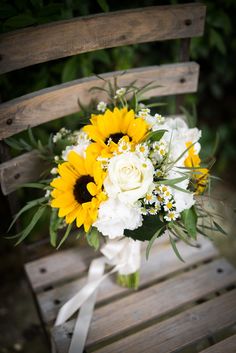 a bouquet of sunflowers and white carnations sits on a wooden bench