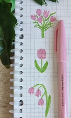 a pink pen sitting on top of a notebook next to a plant