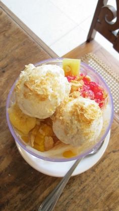 a bowl filled with ice cream and fruit on top of a wooden table next to a chair