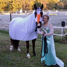 a woman standing next to a horse wearing a white blanket and holding a bridle