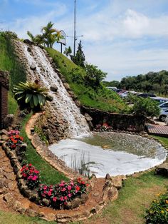 a small waterfall is coming down the side of a hill with flowers growing on it