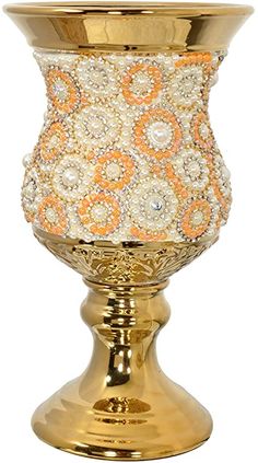 a gold vase with an orange and white design on the top, sitting on a stand