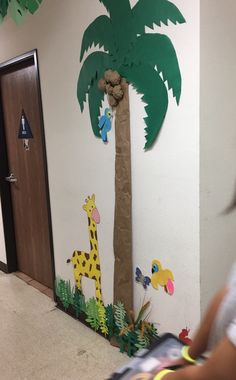 a child's hand holding a cell phone in front of a paper palm tree and giraffe