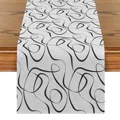 a white table runner with black swirls on it and wood floors in the background