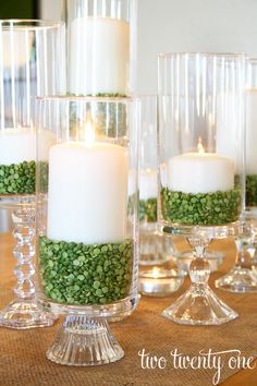 three clear glass vases filled with green beads and white candles sitting on a table