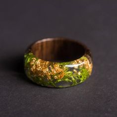 a wooden ring with moss and gold in it on a black surface, close up